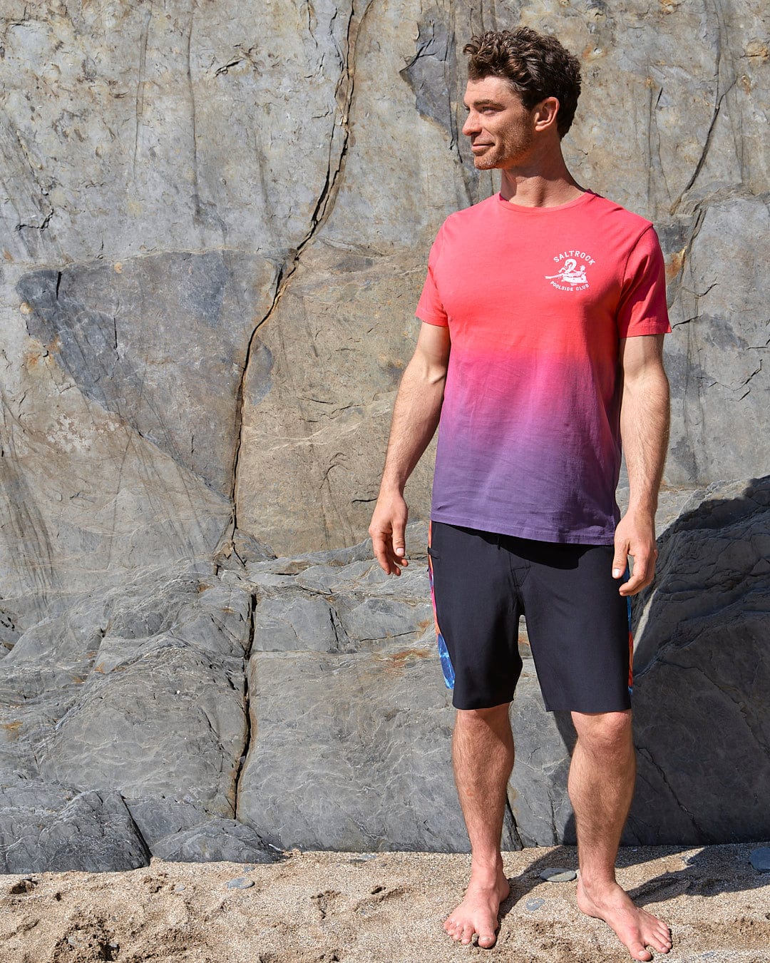 A man in a Poolside - Mens Dip Die Short Sleeve T-Shirt - Pink by Saltrock standing on a rock.
