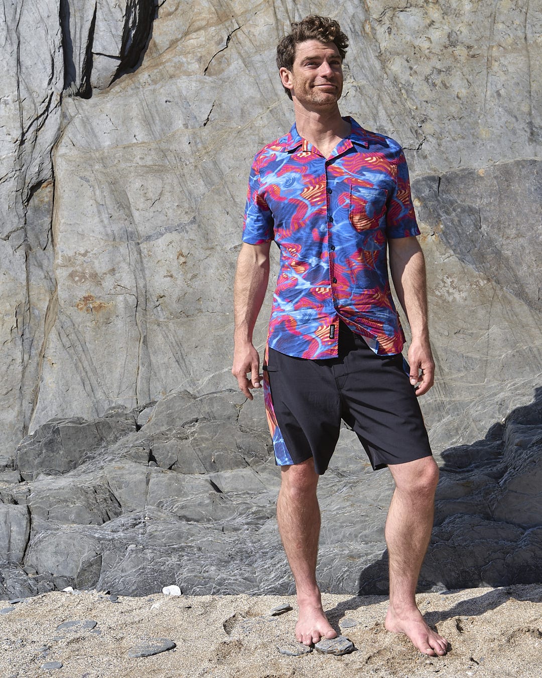 A man standing in front of a Saltrock Poolside Panel - Mens Recycled 4-Way Stretch Boardshort - Black wall.