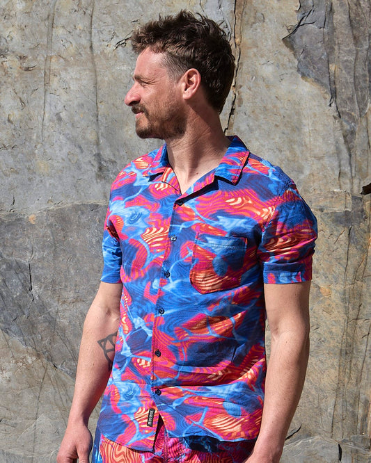 A man in a lightweight Saltrock Poolside - Mens Short Sleeve shirt, with a bright and fun style, standing next to a rock.