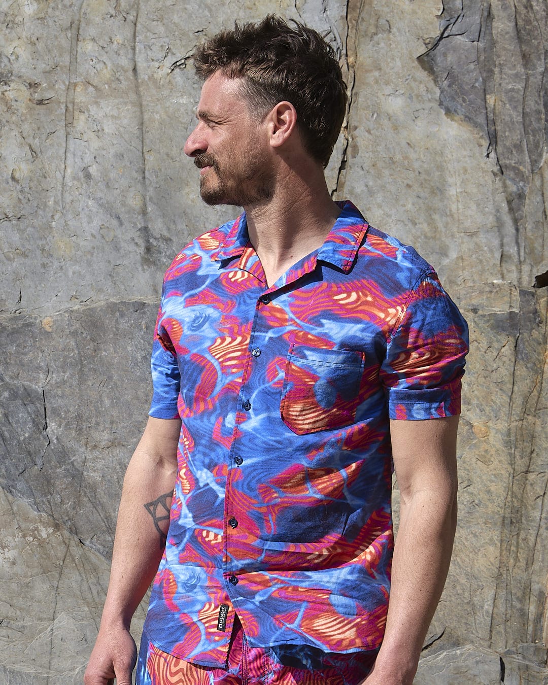 A man in a Saltrock - Poolside - Mens Short Sleeve Shirt - Teal standing next to a rock.