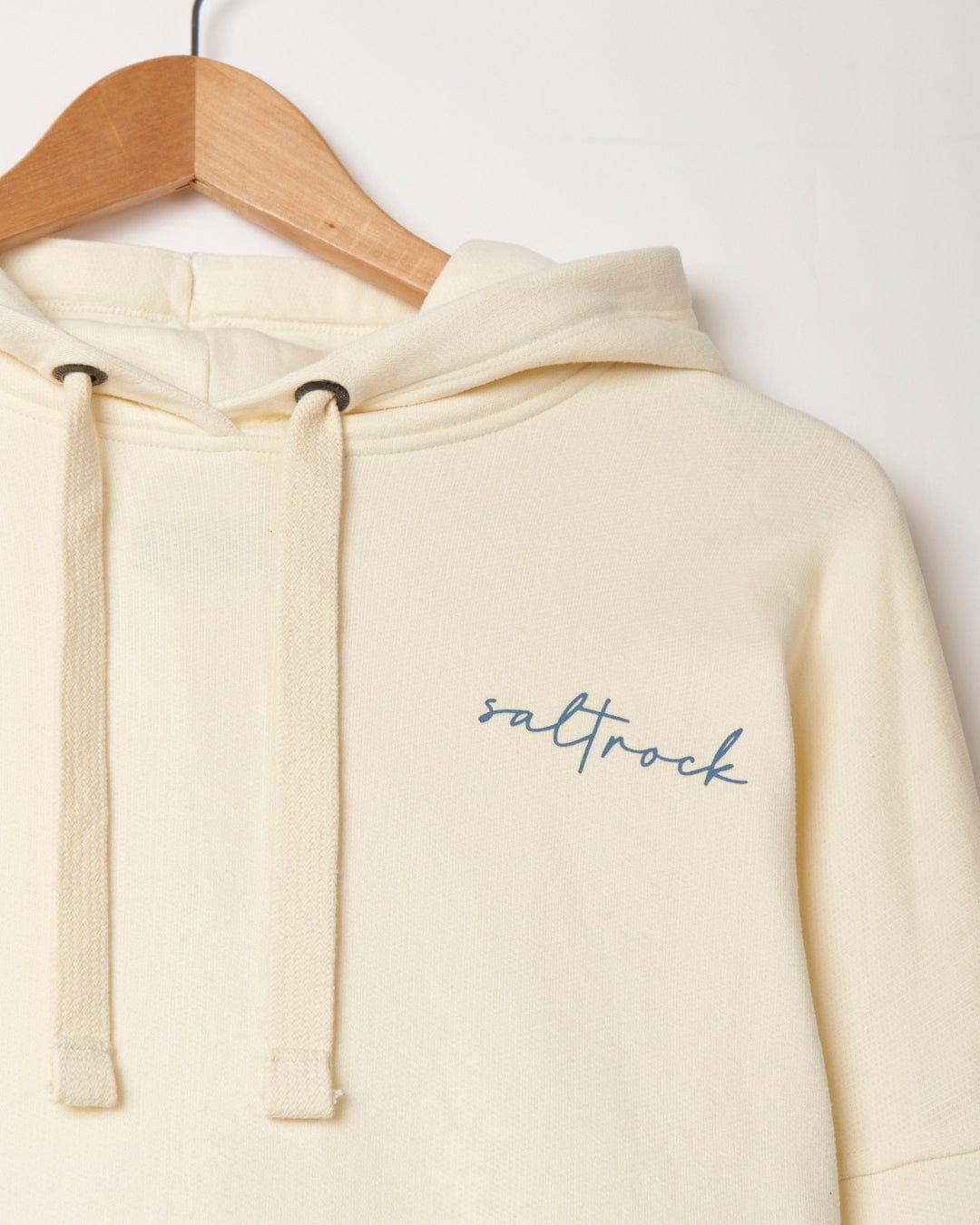 Poster - Womens Pop Hoodie - Cream with Saltrock branding in cursive logo embroidery hanging on a wooden hanger against a white background.