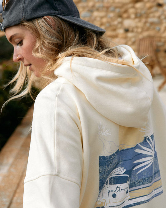 Woman in a Poster - Womens Pop Hoodie in Cream by Saltrock branding and a graphic print, wearing a baseball cap, looking downward.