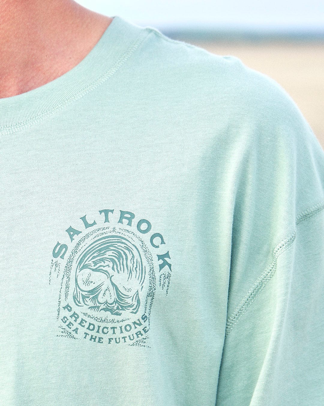 A man wearing a Saltrock Predictions - Mens Long Sleeve T-Shirt - Light Green with skull graphics.