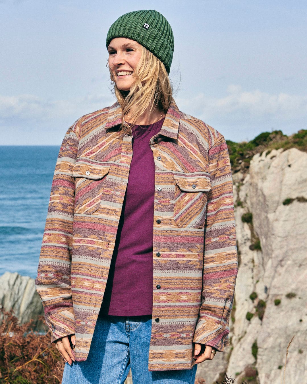 A woman wearing a Saltrock Quinn - Womens Heavy Overshirt - Brown and beanie with Aztec print in front of the ocean.