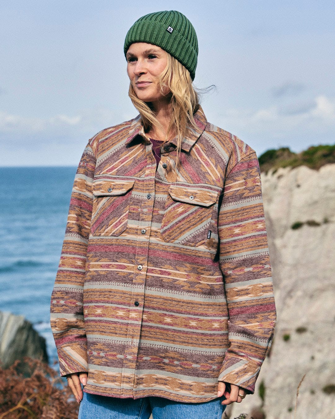 A woman wearing a Saltrock Quinn - Womens Heavy Overshirt - Brown jacket is standing in front of the ocean.