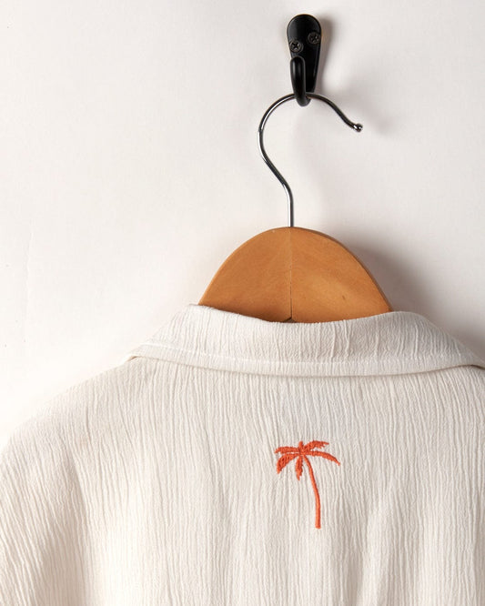 Orange Raya Kids Shirt from Saltrock hanging on a wooden hanger with a small palm tree embroidery on the back.