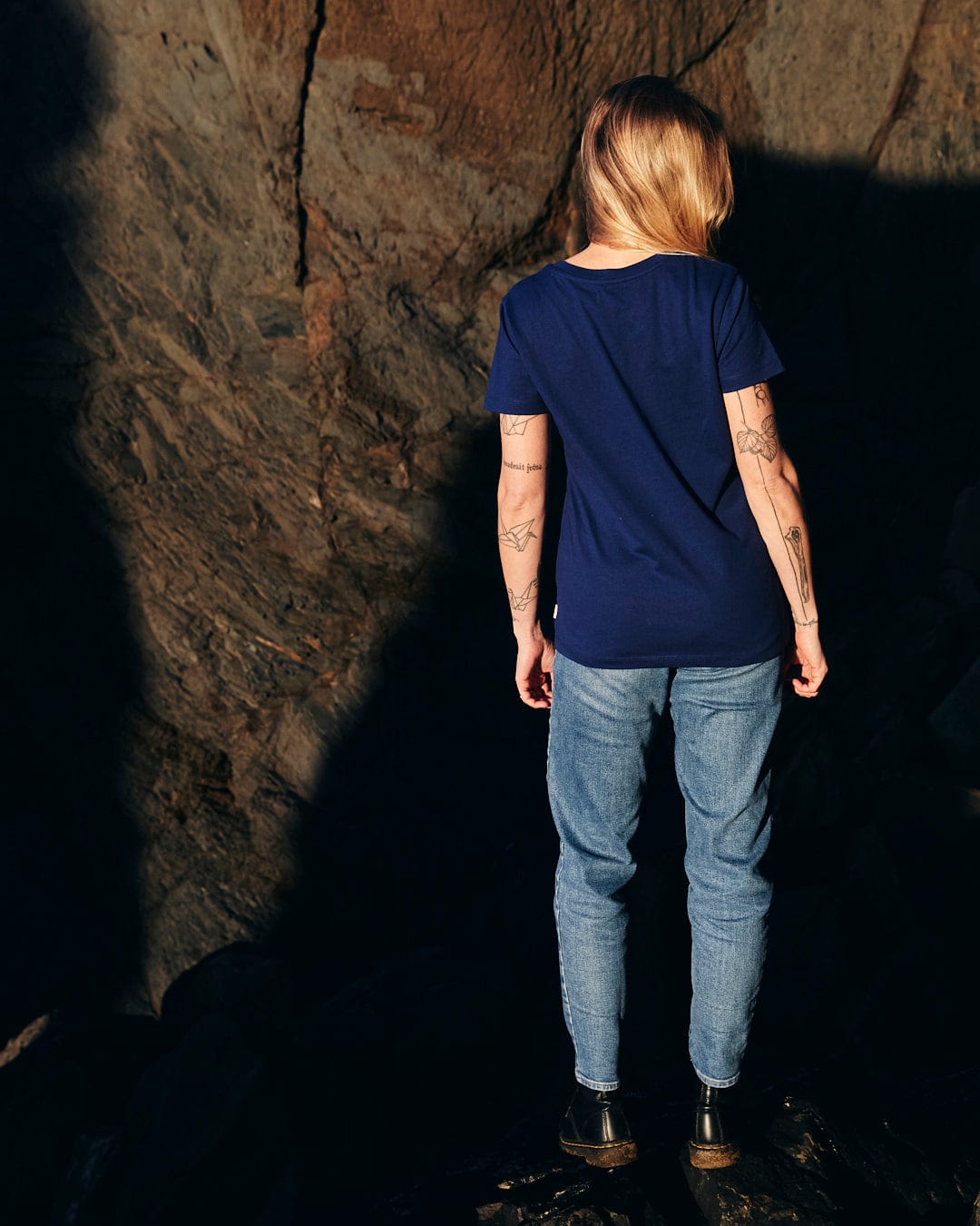 A woman wearing a Saltrock Retro Ribbon - Womens Short Sleeve T-Shirt - Dark Blue standing on a rock.