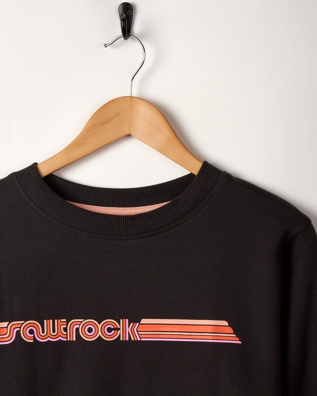 Black crew neck sweatshirt with "Retro Ribbon Tape" text displayed on a wooden hanger against a white background.