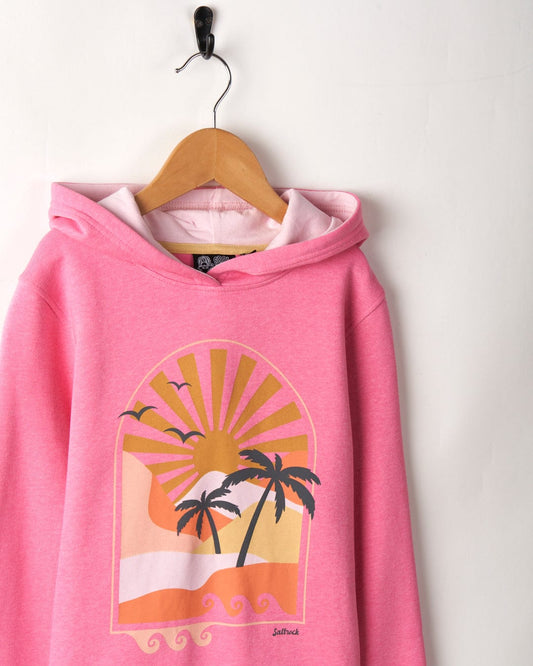 A Retro Seascape - Recycled Kids Longline Pop Hoodie - Pink, featuring Saltrock branding, hangs on a wooden hanger against a white wall.