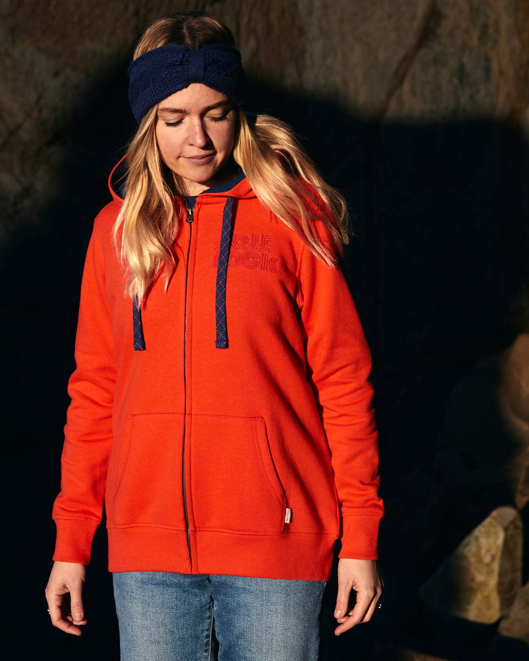 A woman wearing a hat and red jacket with contrast blue hood lining and subtle Saltrock branding, including the Retro Wave Embroidered - Womens Zip Hoodie - Red.