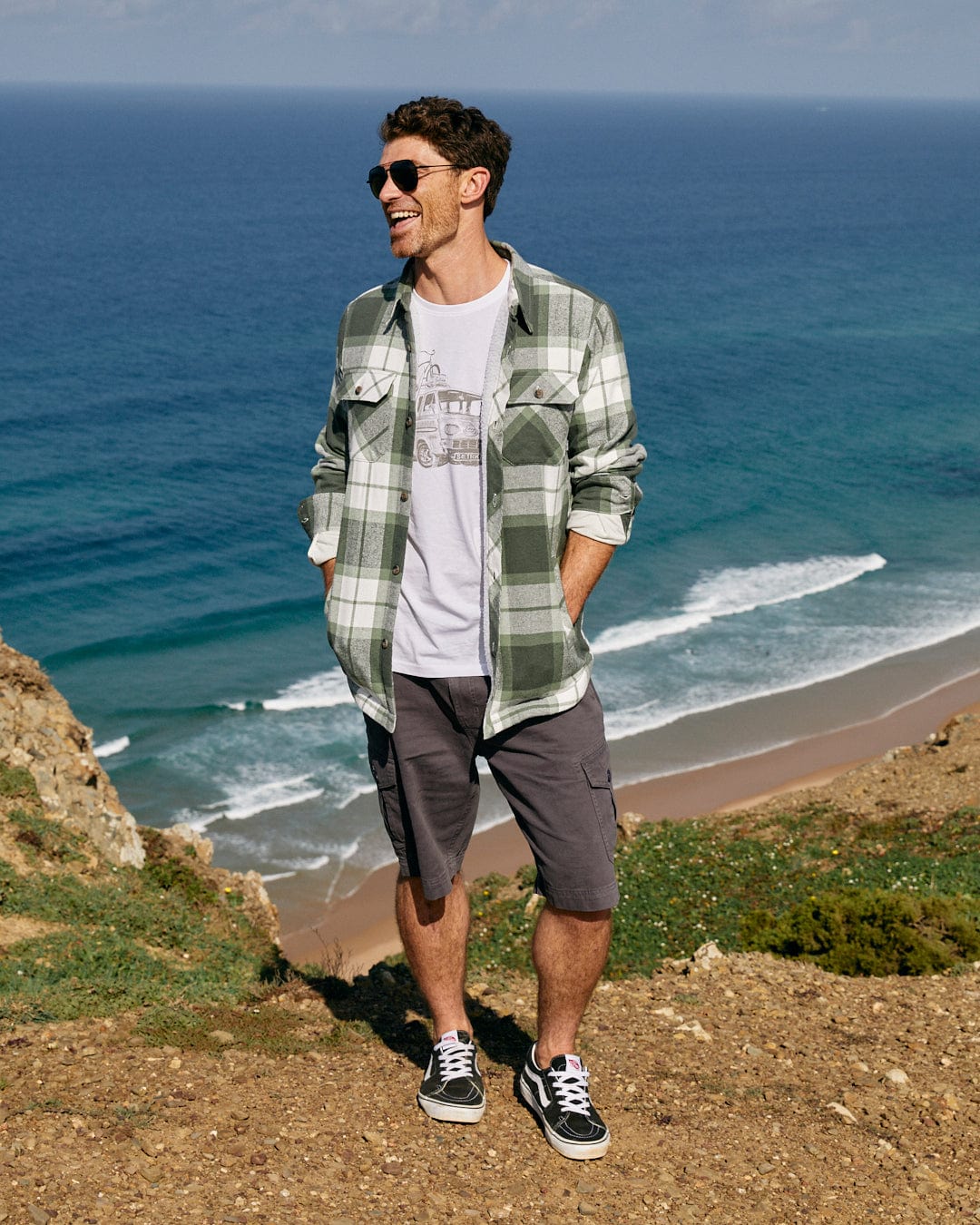 A man standing on a hill next to the ocean, wearing a Saltrock Re-Wild Men's Short Sleeve T-Shirt in White.