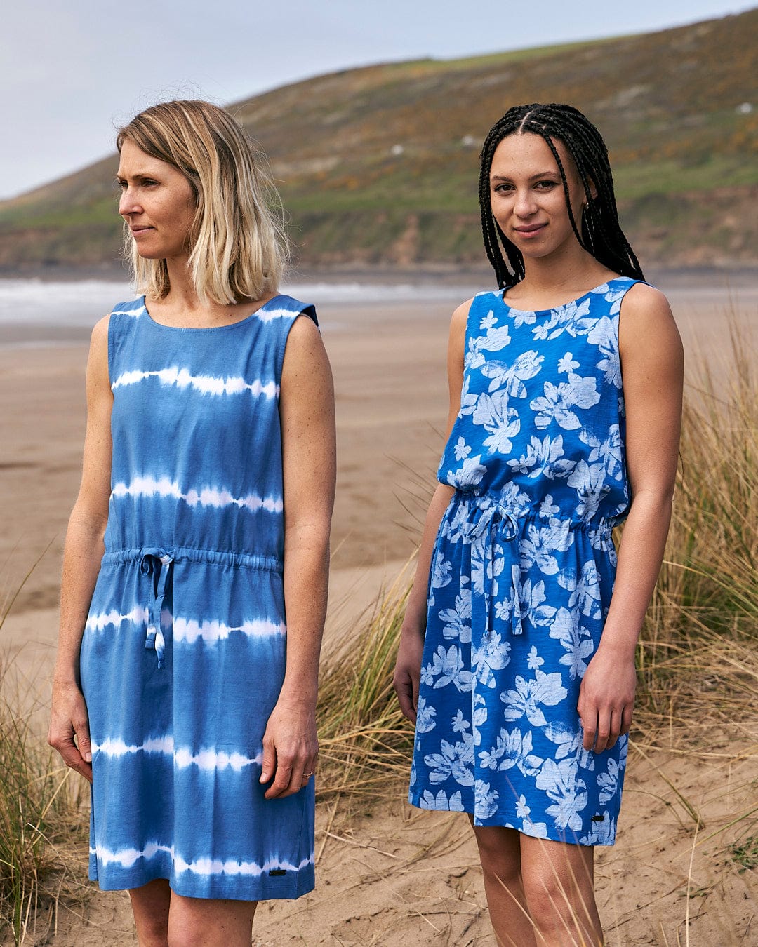 Two women standing next to each other on a beach wearing Saltrock's Floral - Womens Tie Vest Dress in Blue.