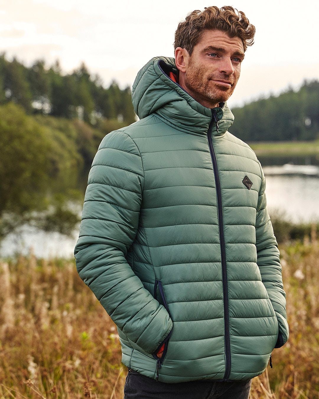 A man in a Saltrock Rusik 2 - Reversible Padded Jacket - Green/Blue standing in a field with water resistance.