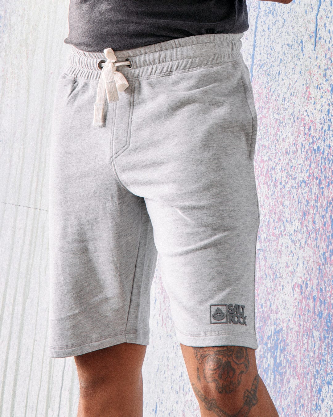 A person stands against a light-colored textured background wearing Saltrock Original Men's Shorts in grey.