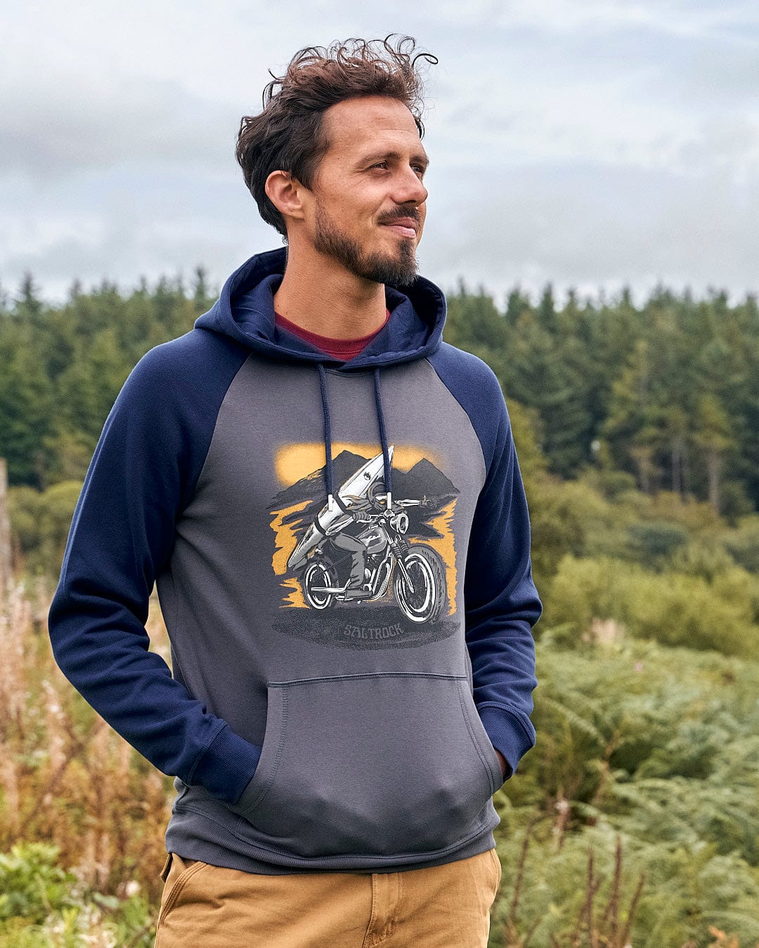 A man wearing a Saltrock Skelly Rider - Mens Pop Hoodie - Dark Grey with a motorcycle graphic on it.