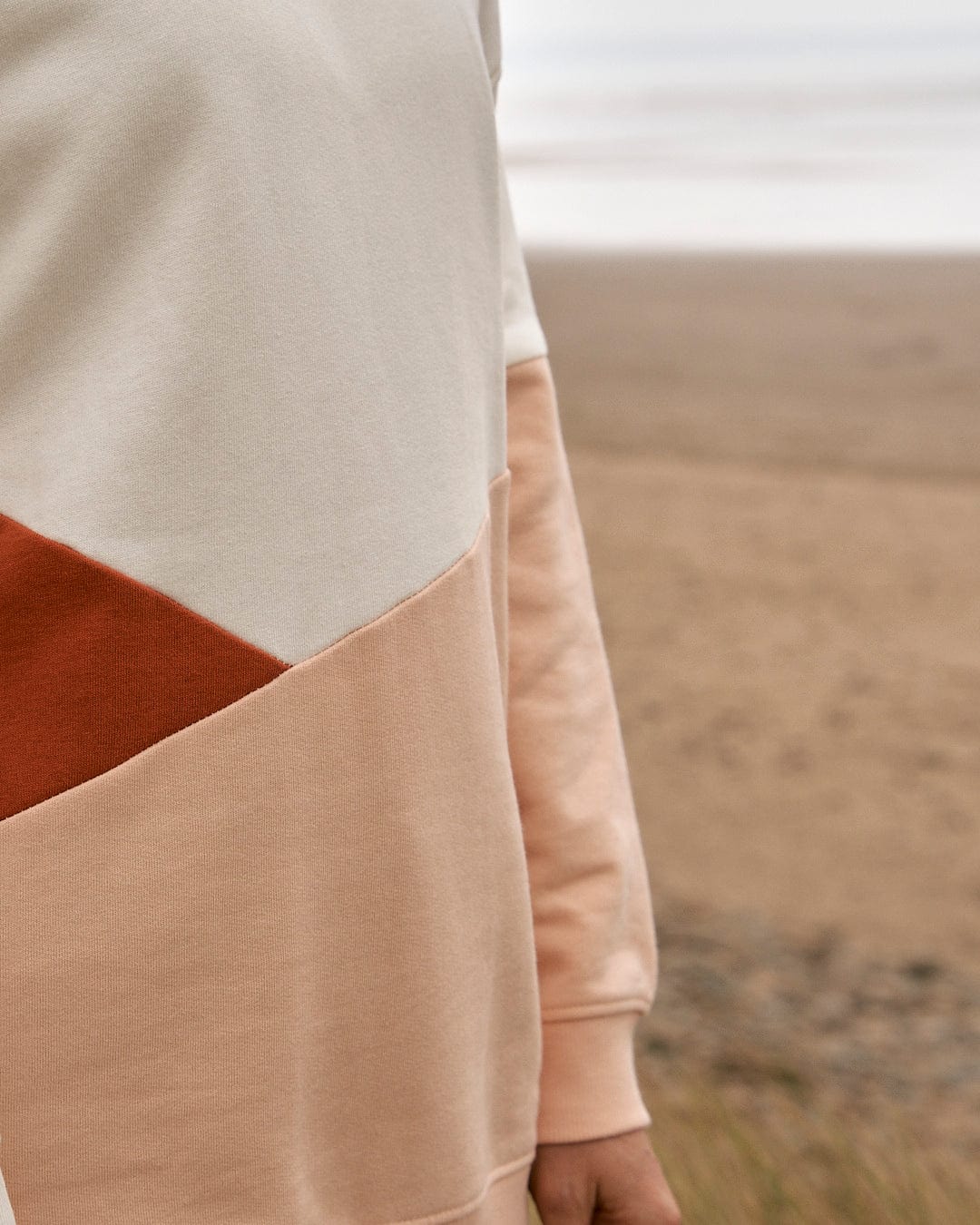 A woman wearing a Saltrock Sofie - Womens Boyfriend Fit Sweat in Light Orange/Cream on the beach.
