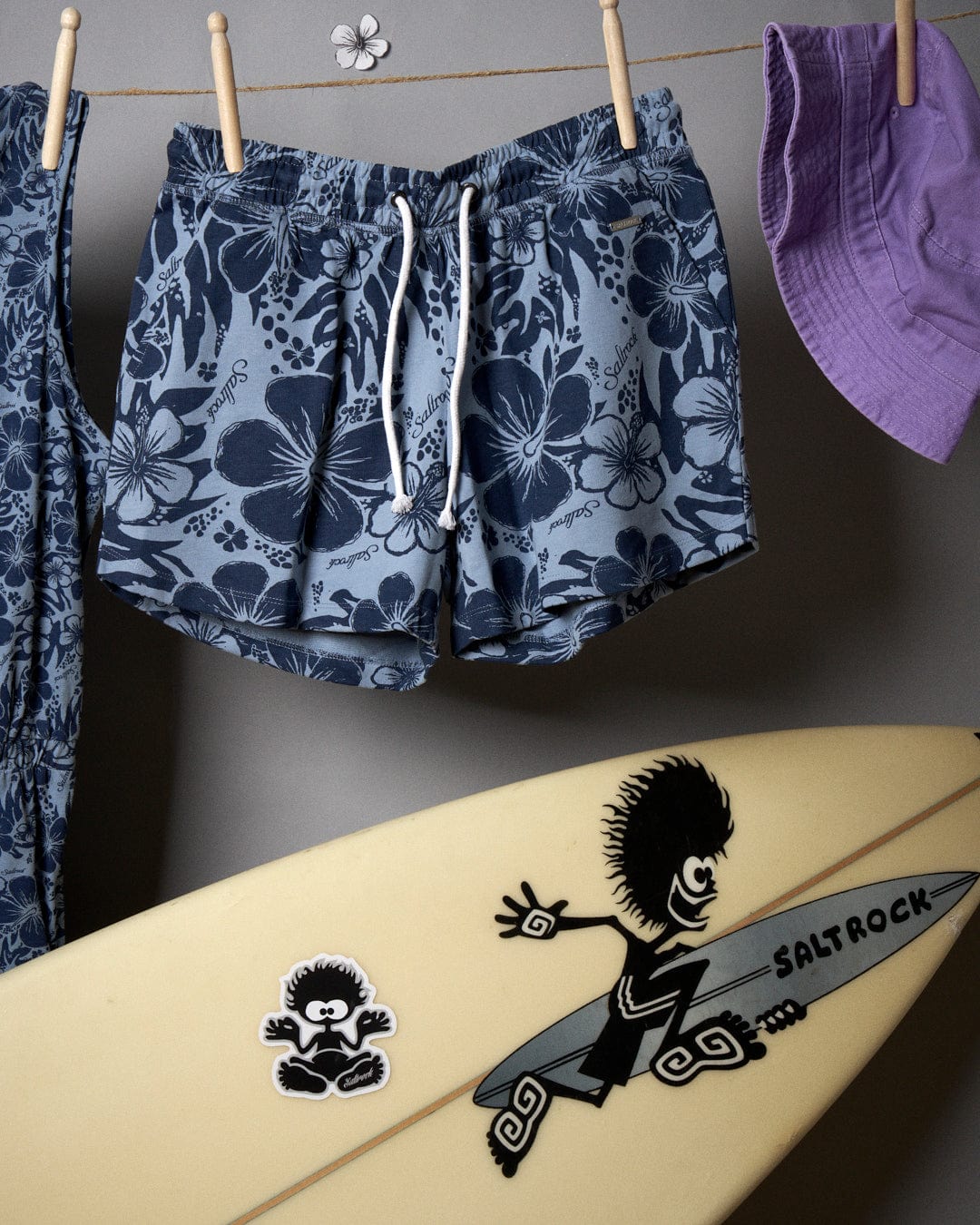 Saltrock Soifra Hibiscus - Womens Sweat Short - Blue short and a surfboard hanging on a clothesline.