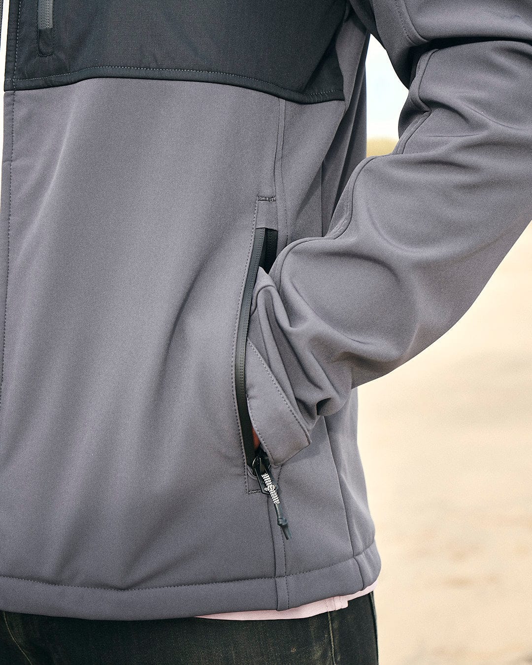 A man in a gray Saltrock Munros - Mens Softshell Jacket - Grey is standing on the beach.