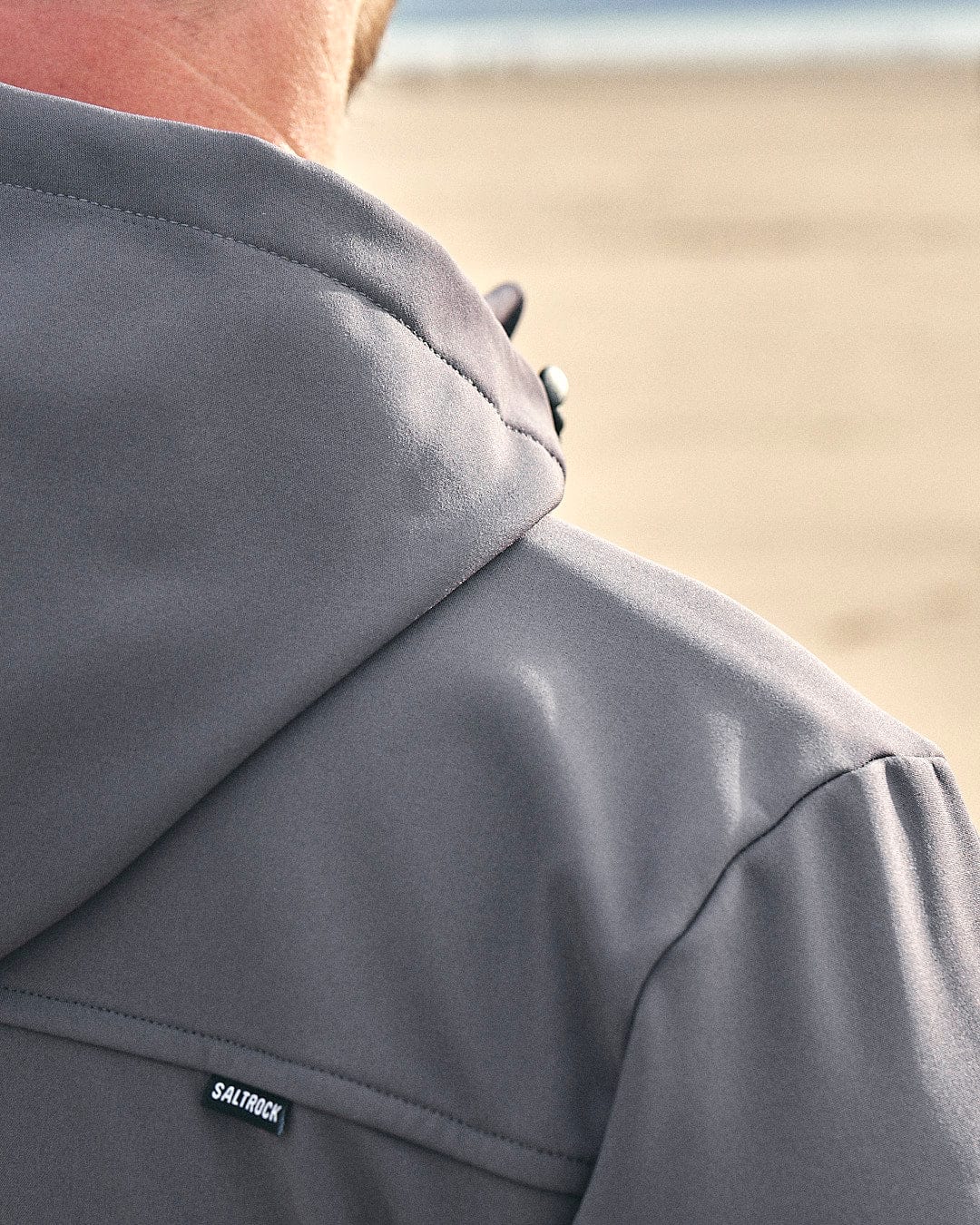 The back of a person wearing a Saltrock Munros - Mens Softshell Jacket - Grey, made with water-resistant fabric and featuring zip pockets.