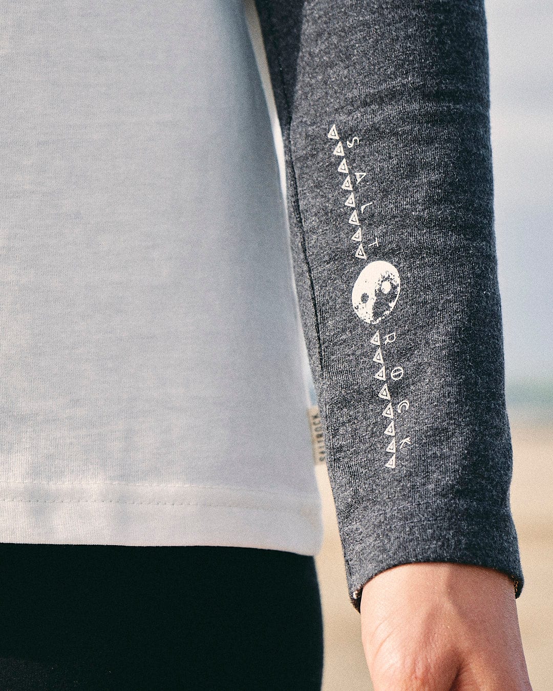 A woman wearing a grey Solstice - Womens Long Sleeve Raglan - Cream shirt with a white Saltrock logo on it.
