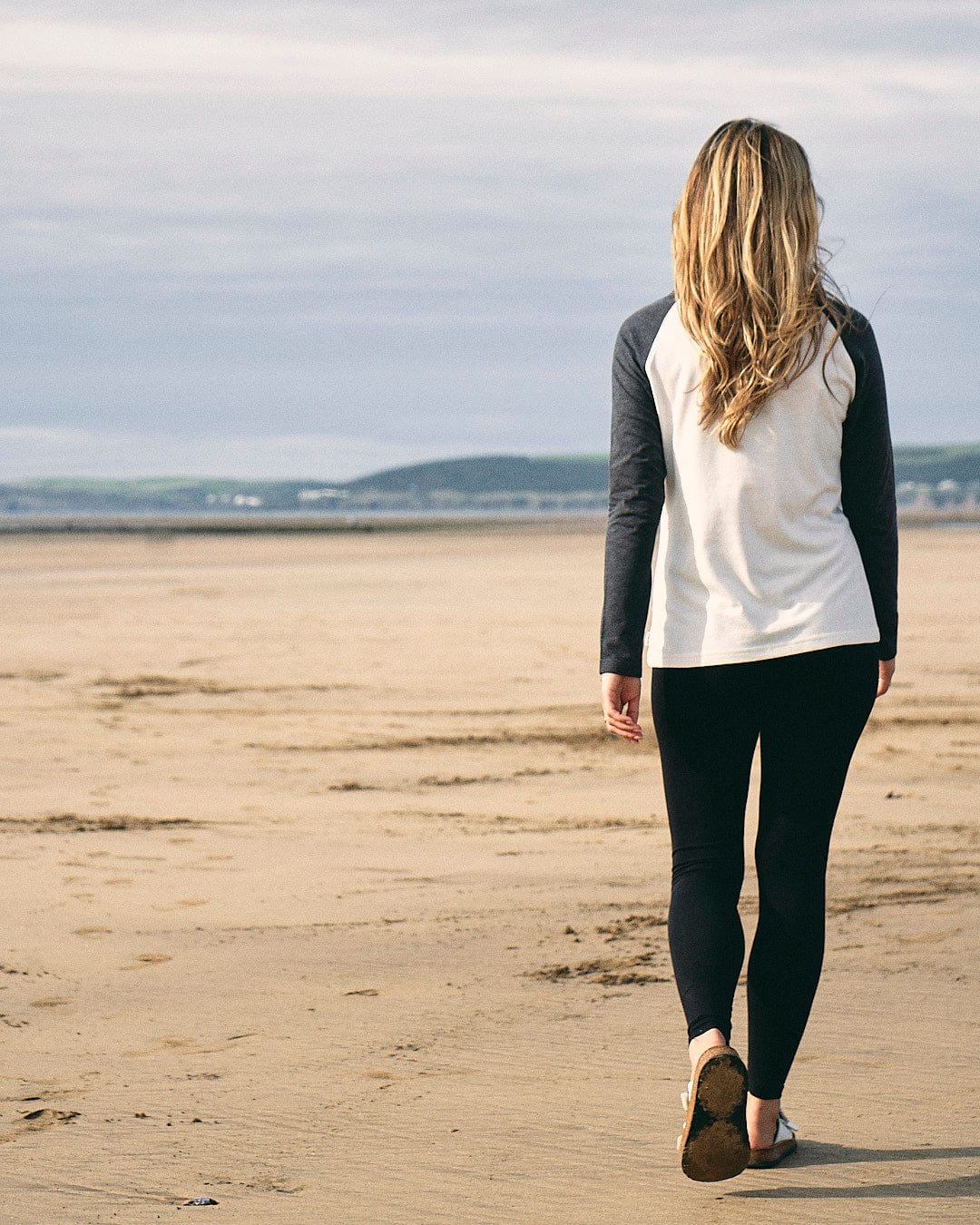 A woman wearing the Saltrock Solstice - Womens Long Sleeve Raglan - Cream walking on the beach.