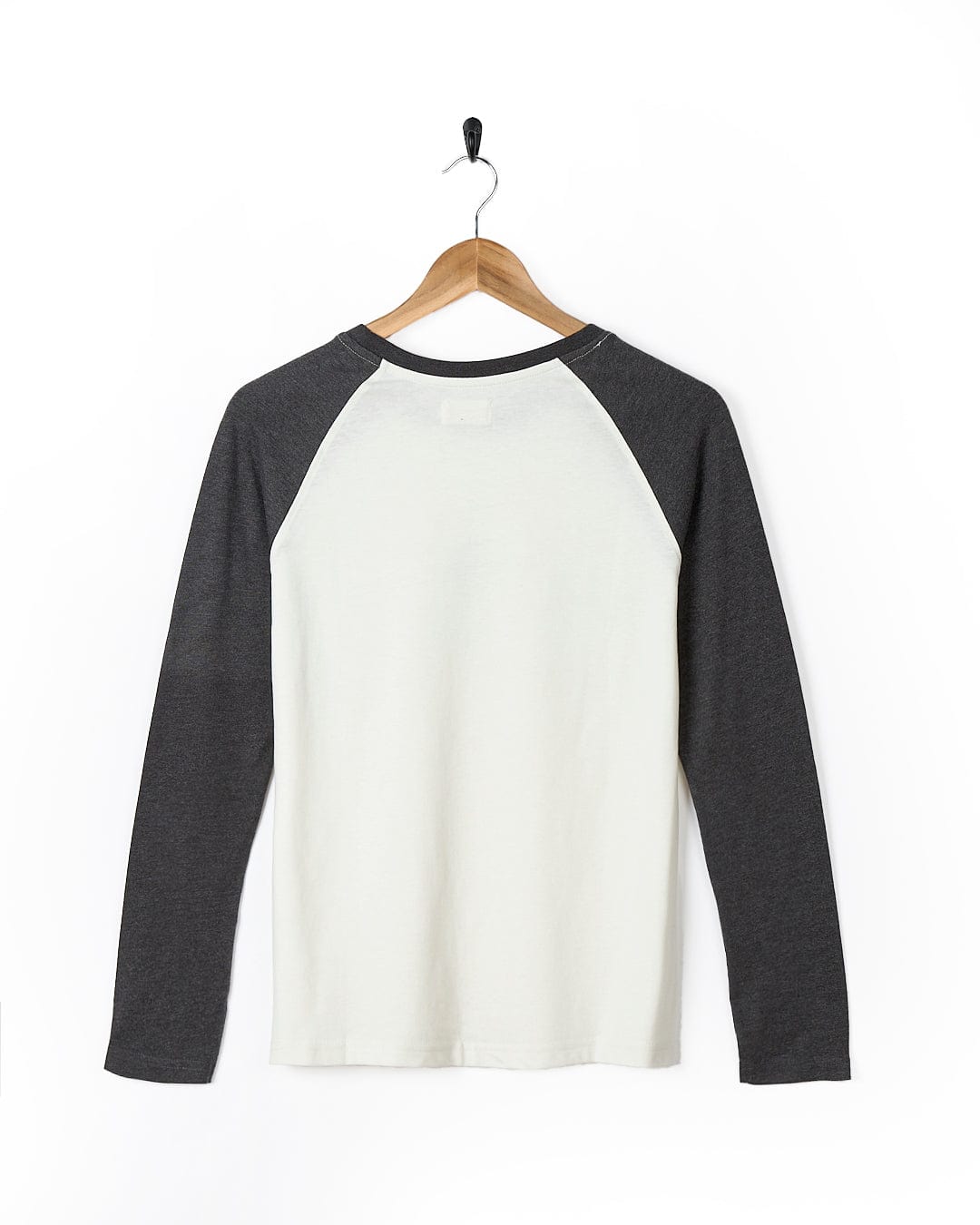 A white and black Solstice - Womens Long Sleeve Raglan - Cream t-shirt hanging on a wooden hanger, Saltrock.