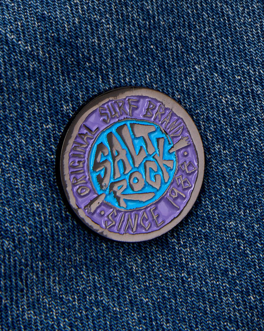 A SR Original pin badge featuring Saltrock graphics, pinned on a denim fabric with a safety clasp.