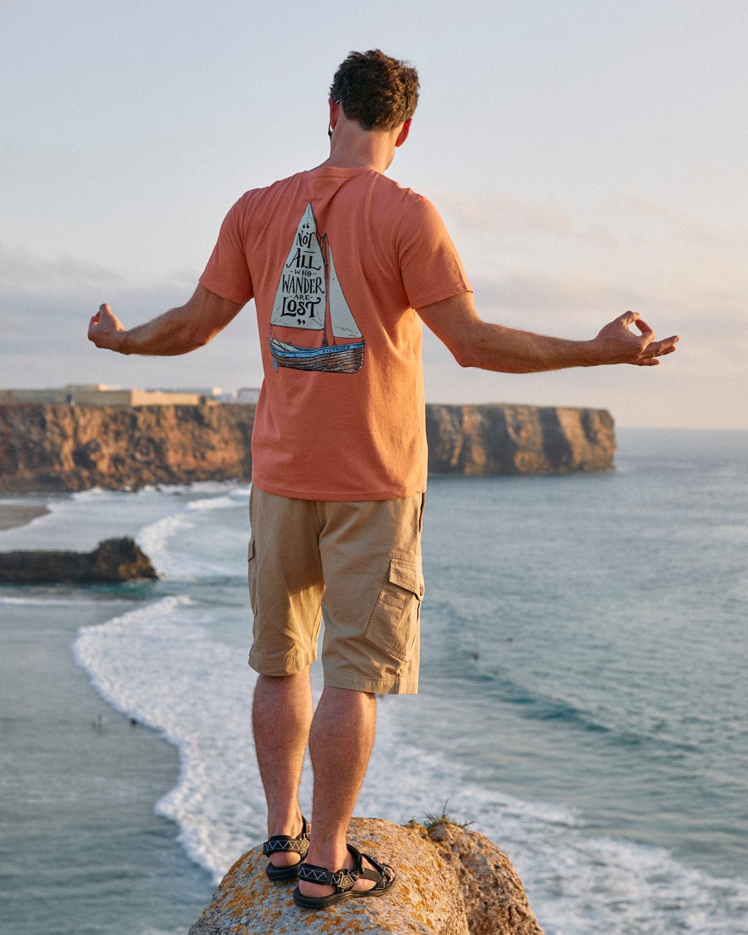 A man standing on top of a cliff overlooking the ocean, wearing a Saltrock Lost Ships classic tee.