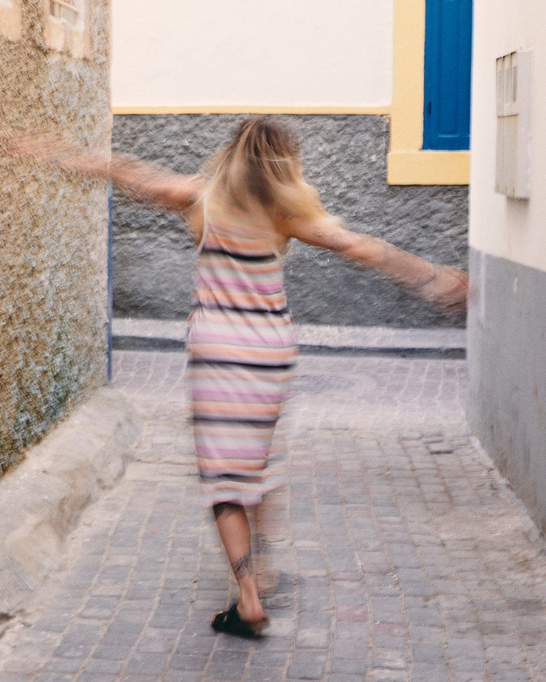 Woman in a Saltrock Juno - Womens Midi Dress - Multi playfully spinning on a cobblestone alley, surrounded by colorful building façades.