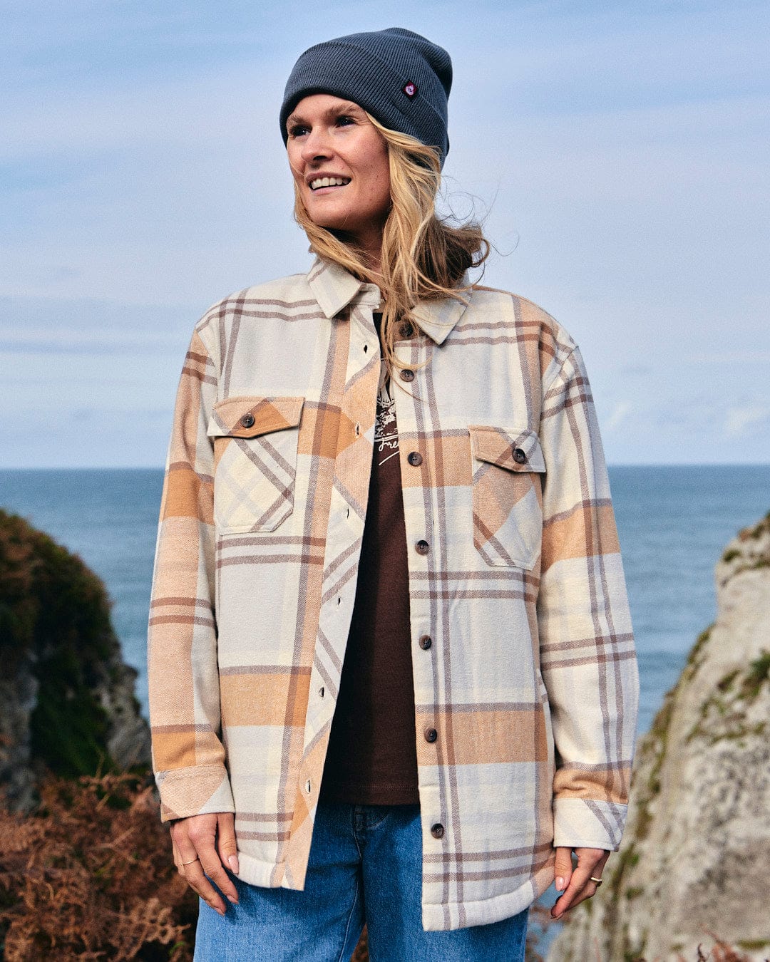 A woman wearing a Saltrock Stella - Womens Checked Borg Lined Shacket - Cream, featuring buttoned cuffs and Borg lined detailing.