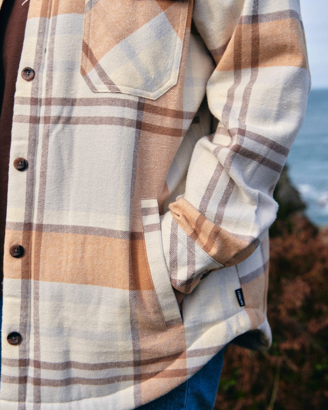 A man wearing a Saltrock Stella - Womens Checked Borg Lined Shacket - Cream near the ocean.