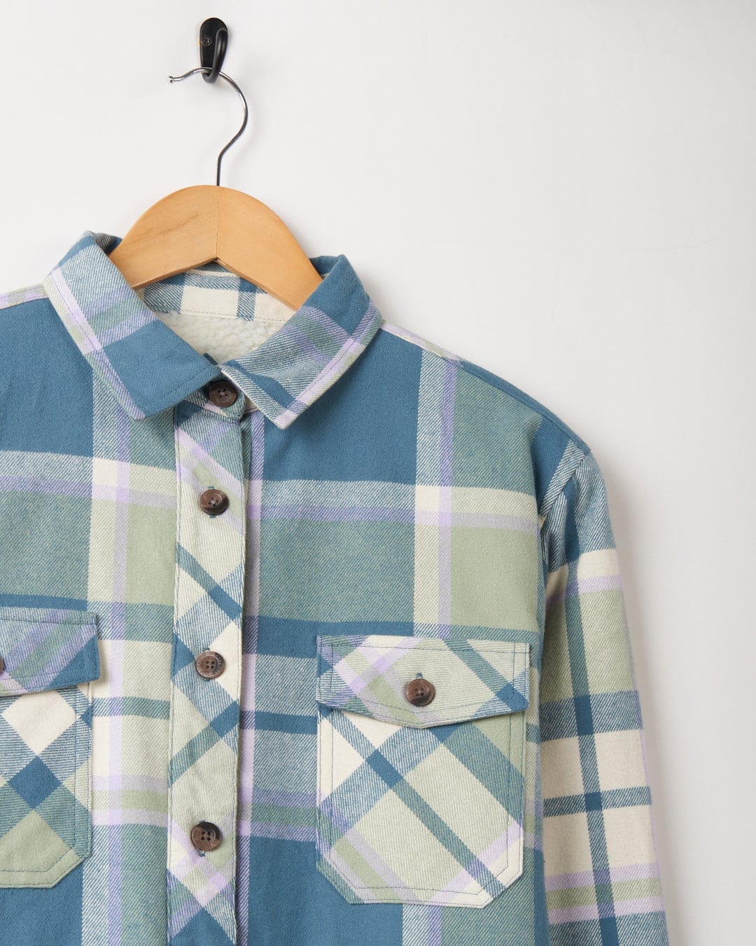 A Stella - Womens Borg Lined Long Sleeve Shirt in shades of blue and green hanging on a wooden hanger against a white background.