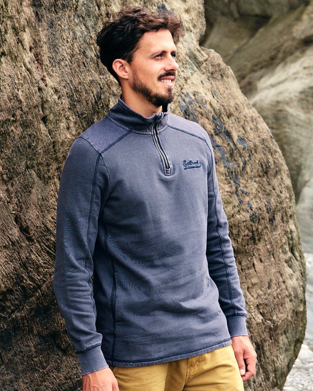 A fashionable man is standing next to a Stellan - Mens 1/4 Neck Sweat - Grey Acid Wash by Saltrock by the ocean.