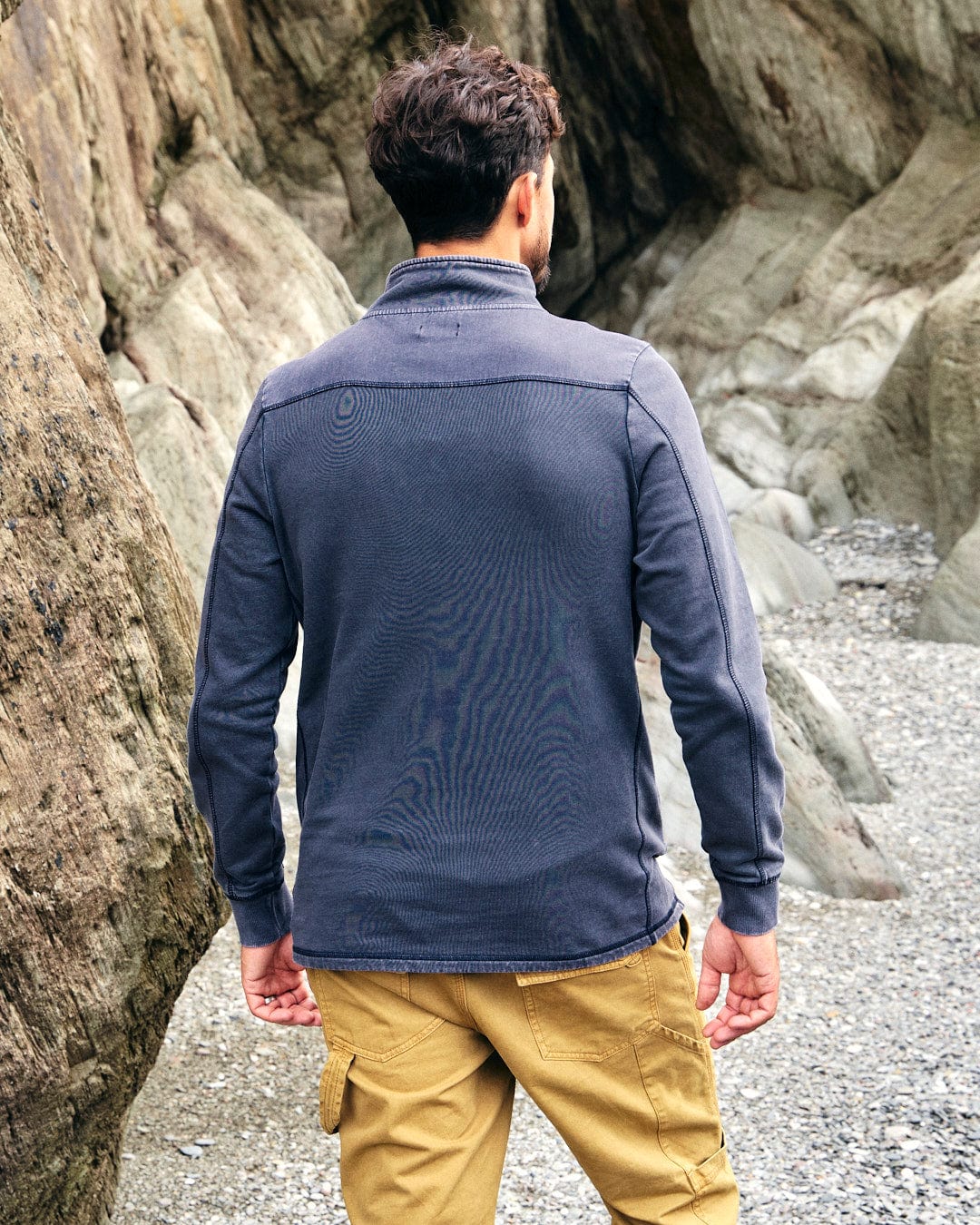 A man is standing in front of rocks wearing Saltrock's Stellan - Mens 1/4 Neck Sweat - Grey Acid Wash sweatpants.