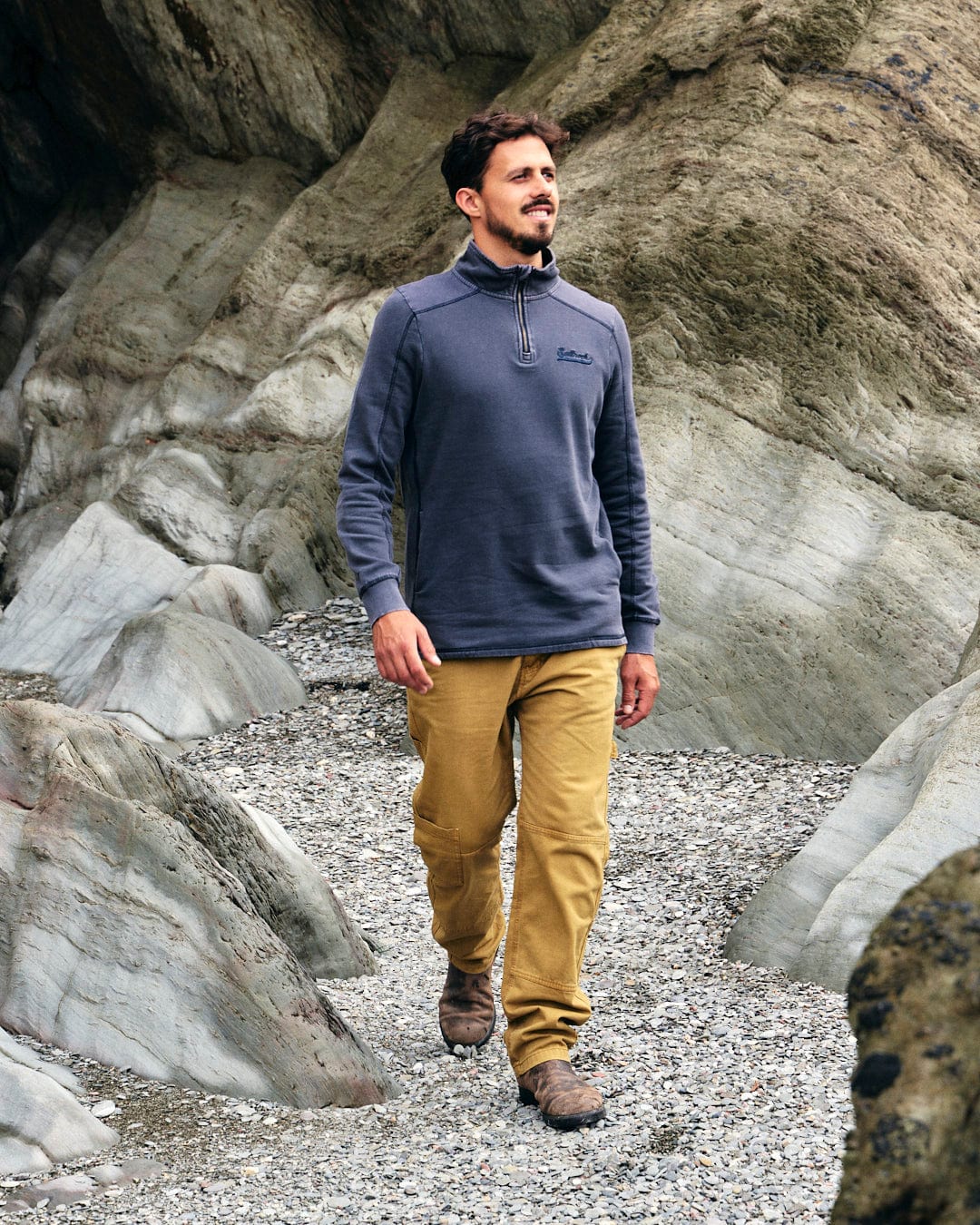 A man fashionably walking on a rocky path wearing a Stellan - Mens 1/4 Neck Sweat - Grey Acid Wash by Saltrock.