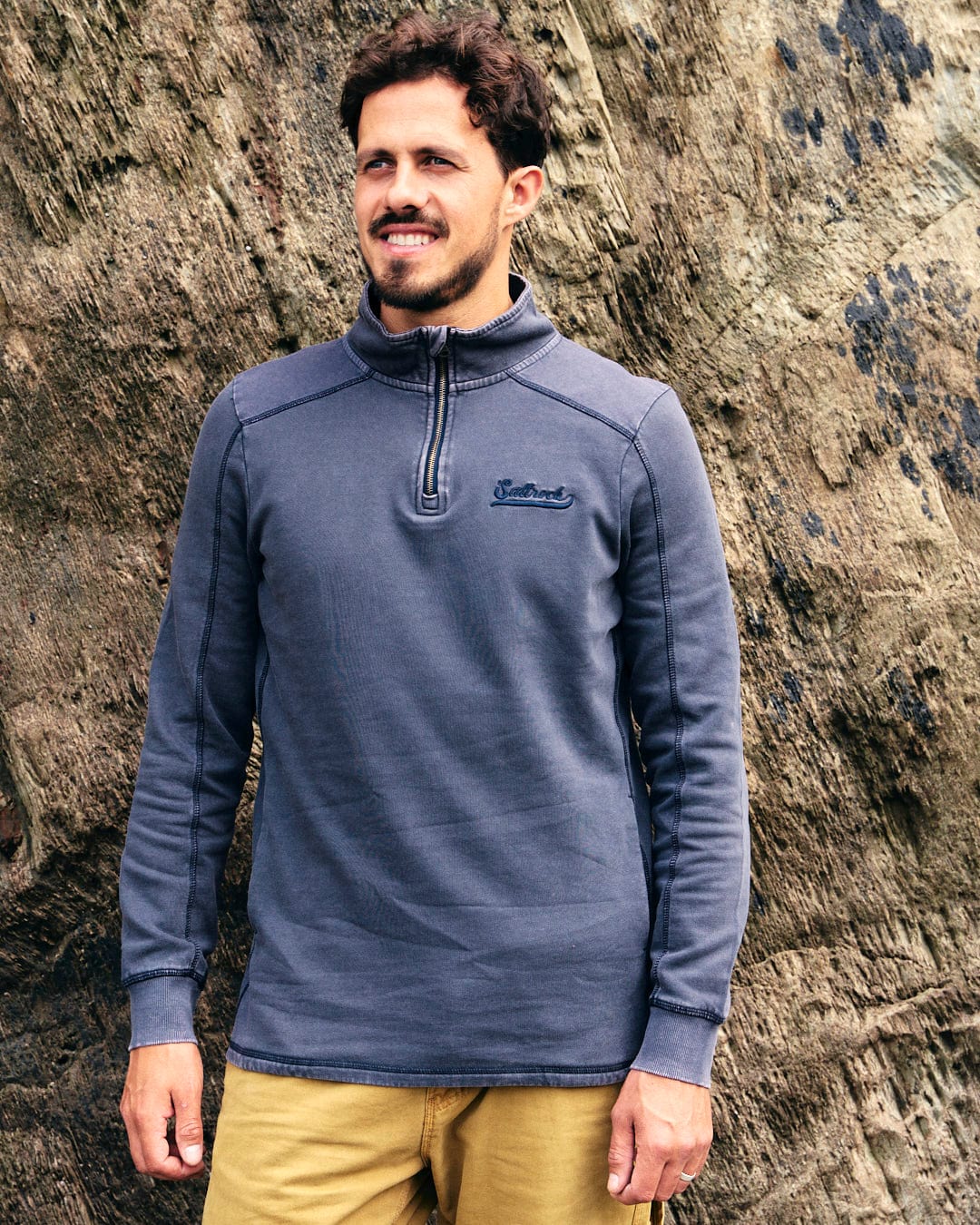 A man in fashionable Saltrock Stellan - Mens 1/4 Neck Sweat - Grey Acid Wash attire stands in front of a rock.