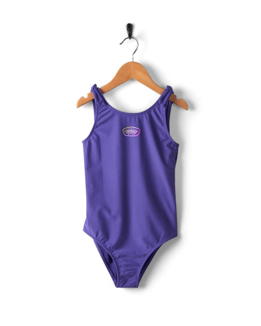 A Saltrock purple kids full piece swimsuit hanging on a wooden hanger against a white background.