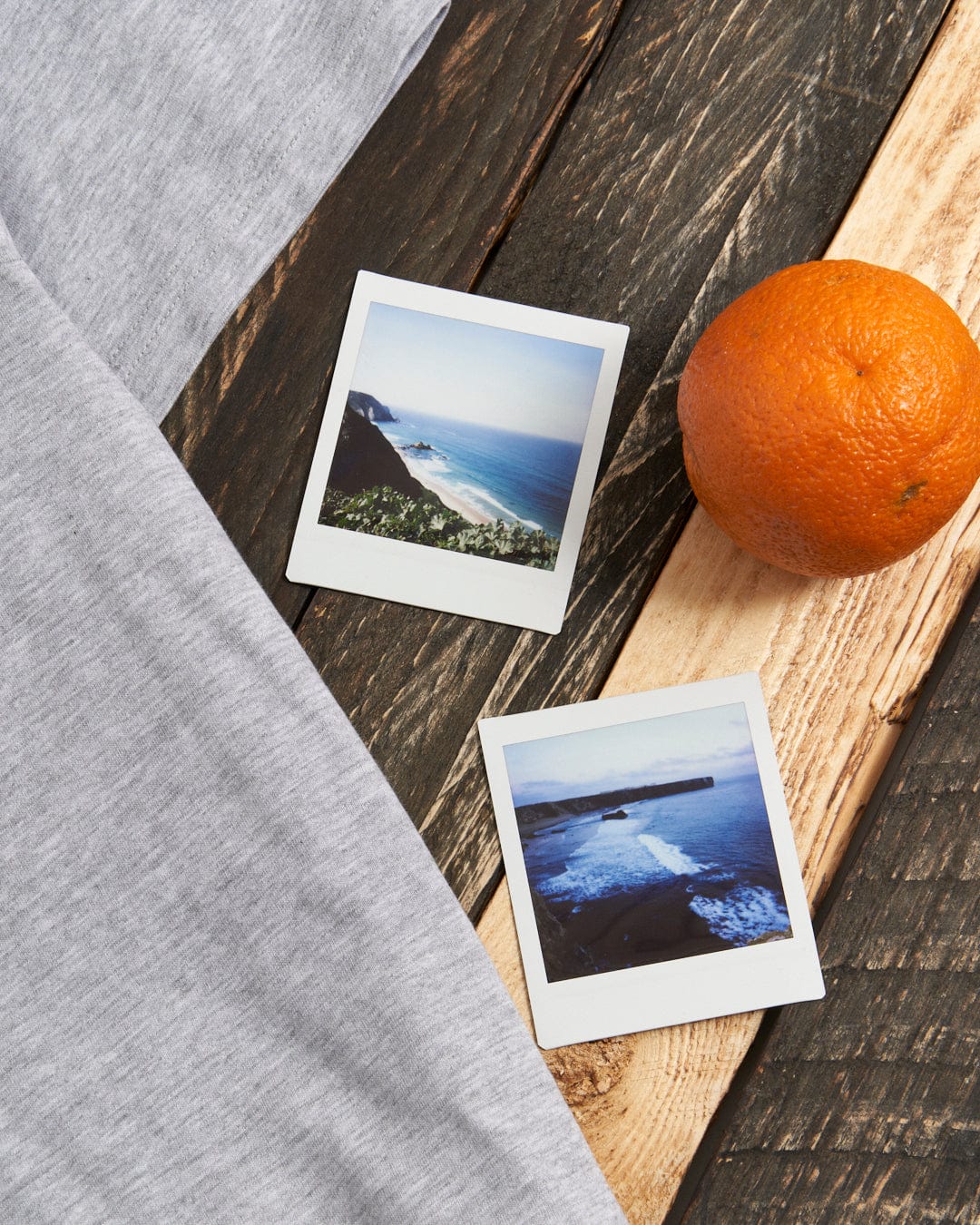 A Saltrock Sun Sets - Mens Short Sleeve T-Shirt - Grey Marl and an orange on a wooden table.