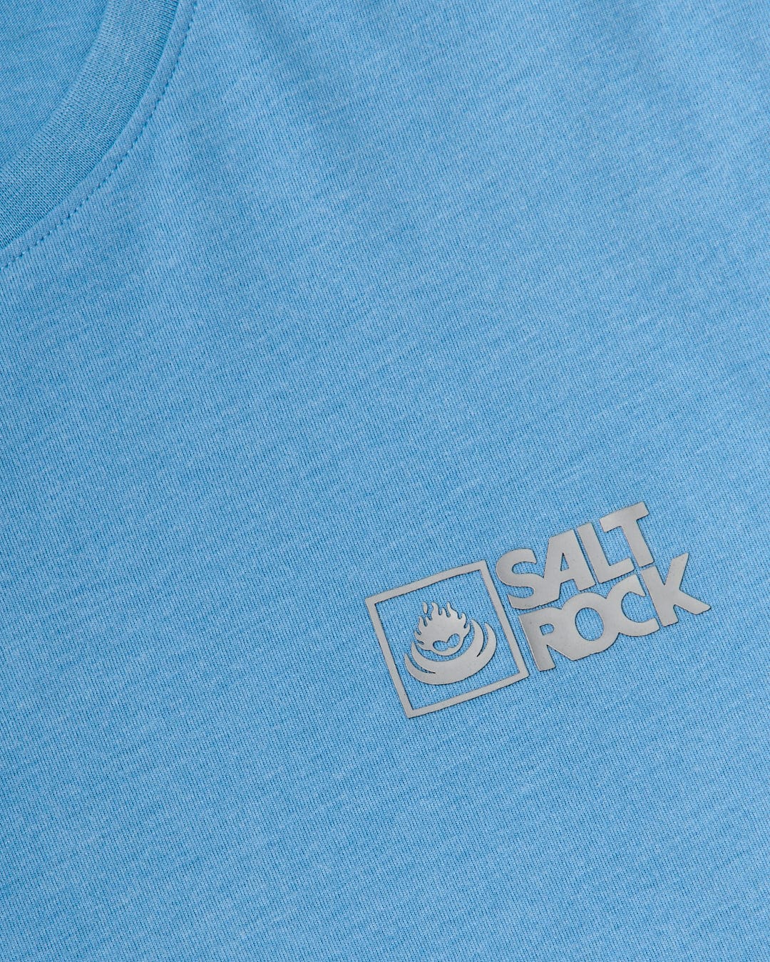 Close-up of a blue lightweight material texture with a Saltrock Original - Mens Short Sleeve T-Shirt - Light Blue logo embroidered in white on the left side.