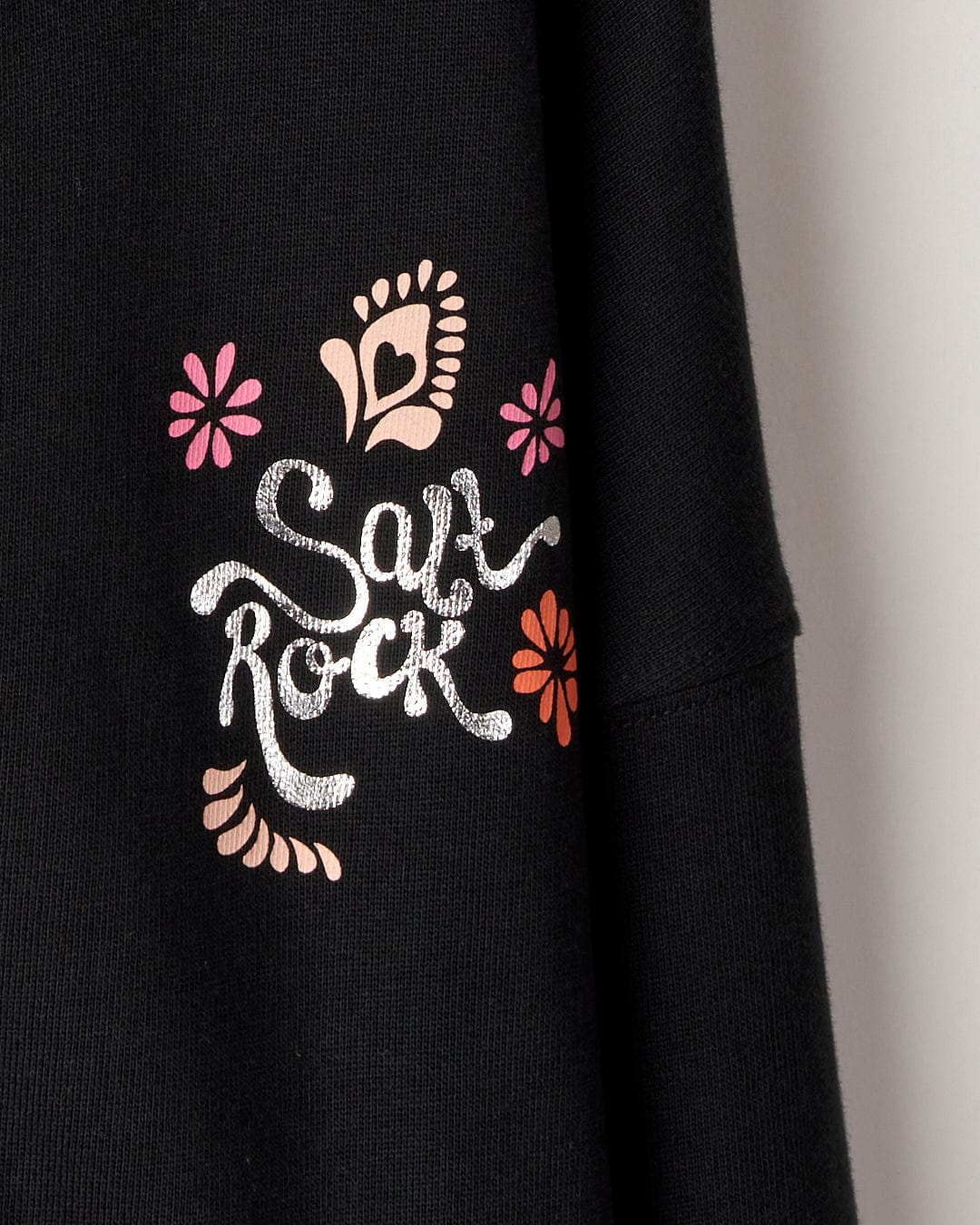Close-up of a Tahiti Van Kids Zip Hoodie in Washed Black by Saltrock with a glittery silver "sax rock" text and graphic design including a saxophone, pink and orange flowers.
