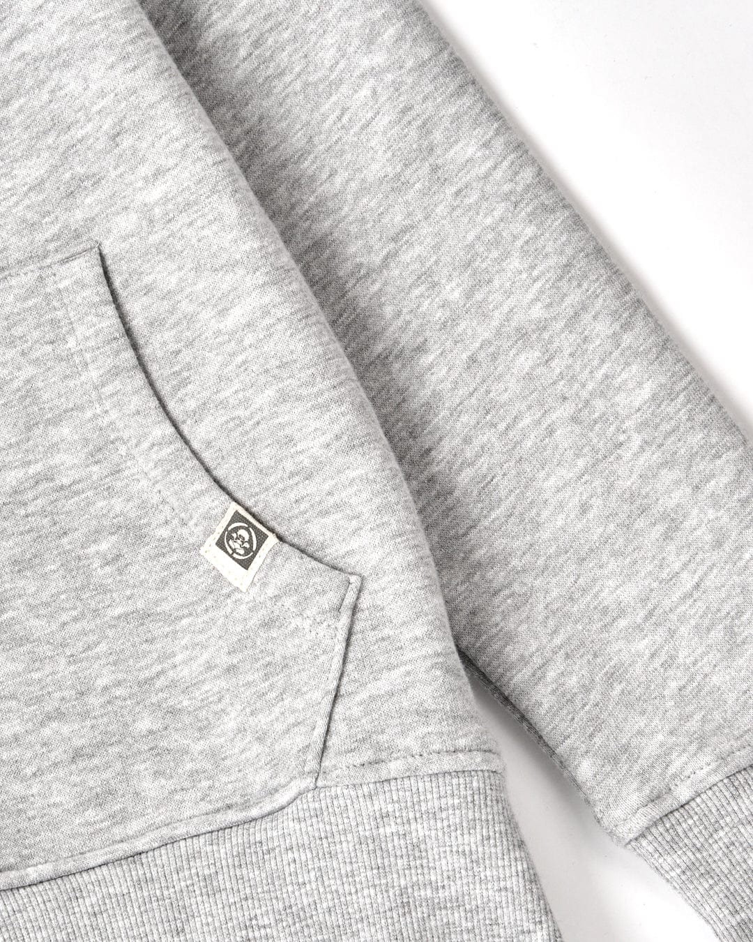 Close-up of a Tok Corp - Recycled Kids Zip Hoodie - Grey Marl with a small Saltrock branding on the chest pocket, alongside gray patterned fabric.
