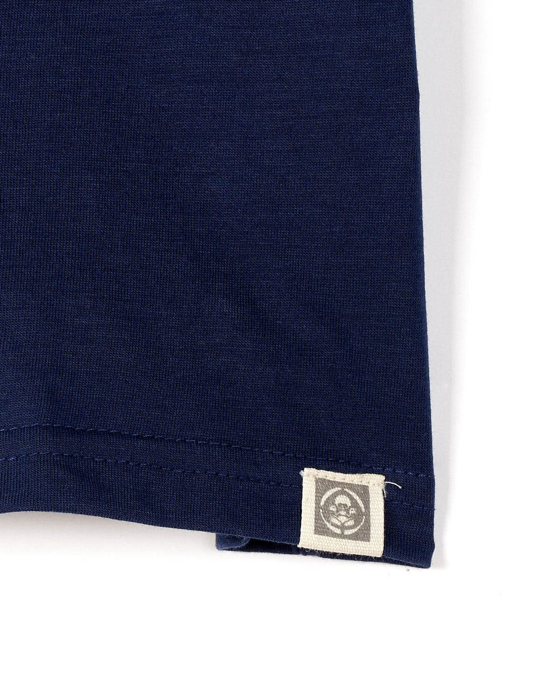 Close-up of a Saltrock Tok Stripe - Kids Short Sleeve T-Shirt in Dark Blue with a small square label showing a recycling symbol, stitched on the hem.