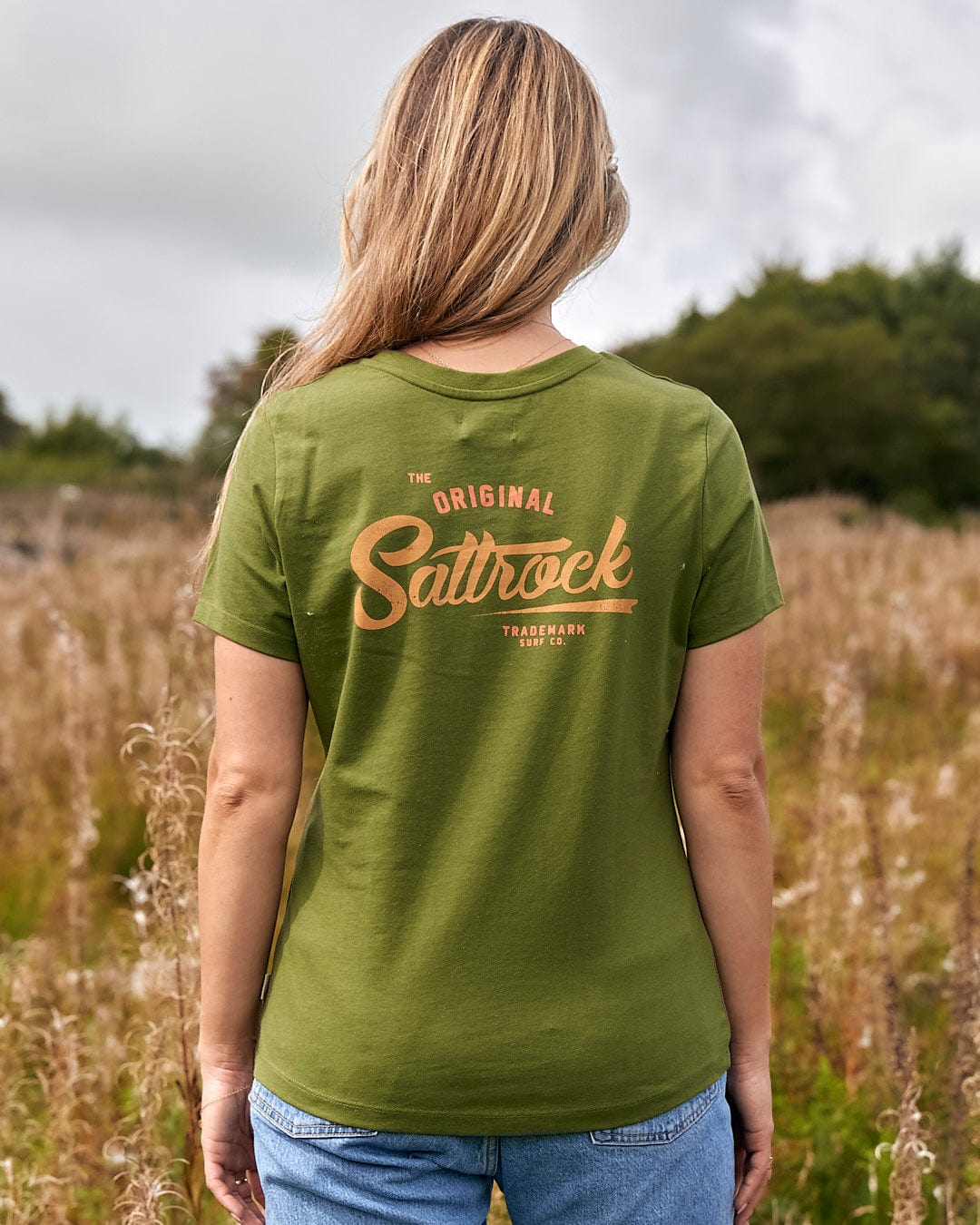 The back of a woman standing in a field wearing a green t-shirt with Saltrock branding. The back of a woman standing in a field wearing a green Trademark - Womens Short Sleeve T-Shirt - Green with Saltrock branding.