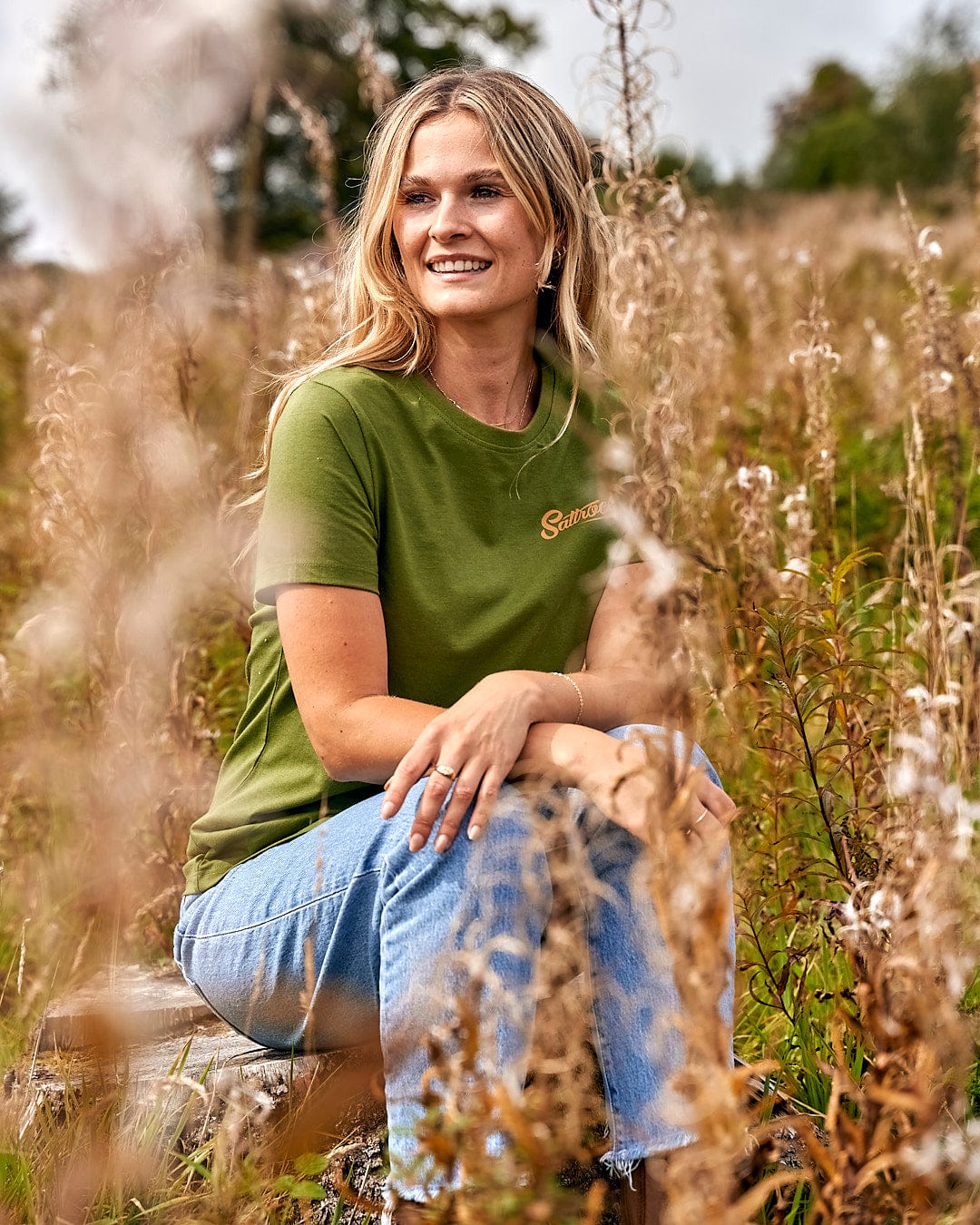 A woman sitting in a field wearing Saltrock Trademark - Womens Short Sleeve T-Shirt - Green.