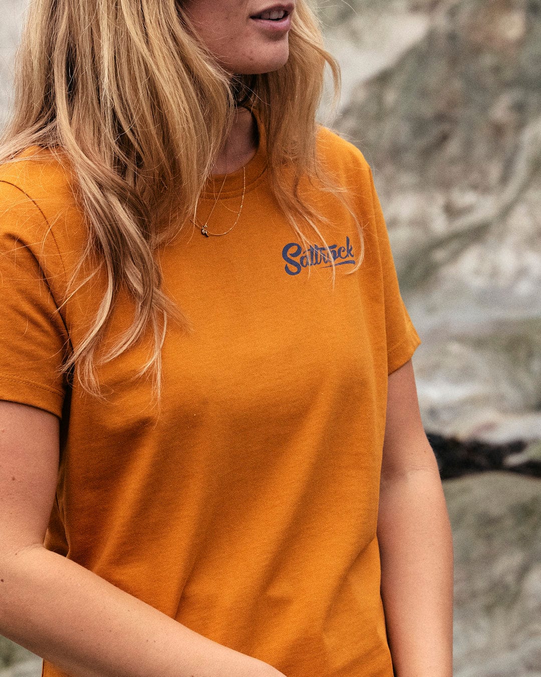 A woman wearing a Saltrock yellow short sleeve t-shirt made of lightweight fabric standing in front of rocks.