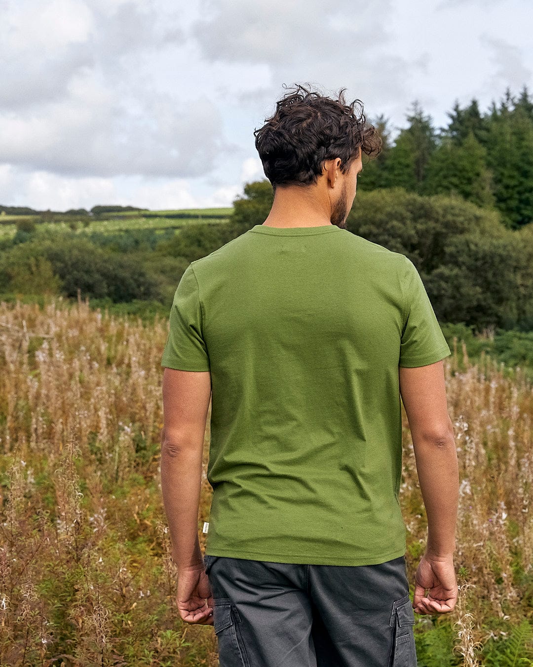 A man wearing a Saltrock Trail Bike - Mens Short Sleeve T-Shirt - Green stands in a field.