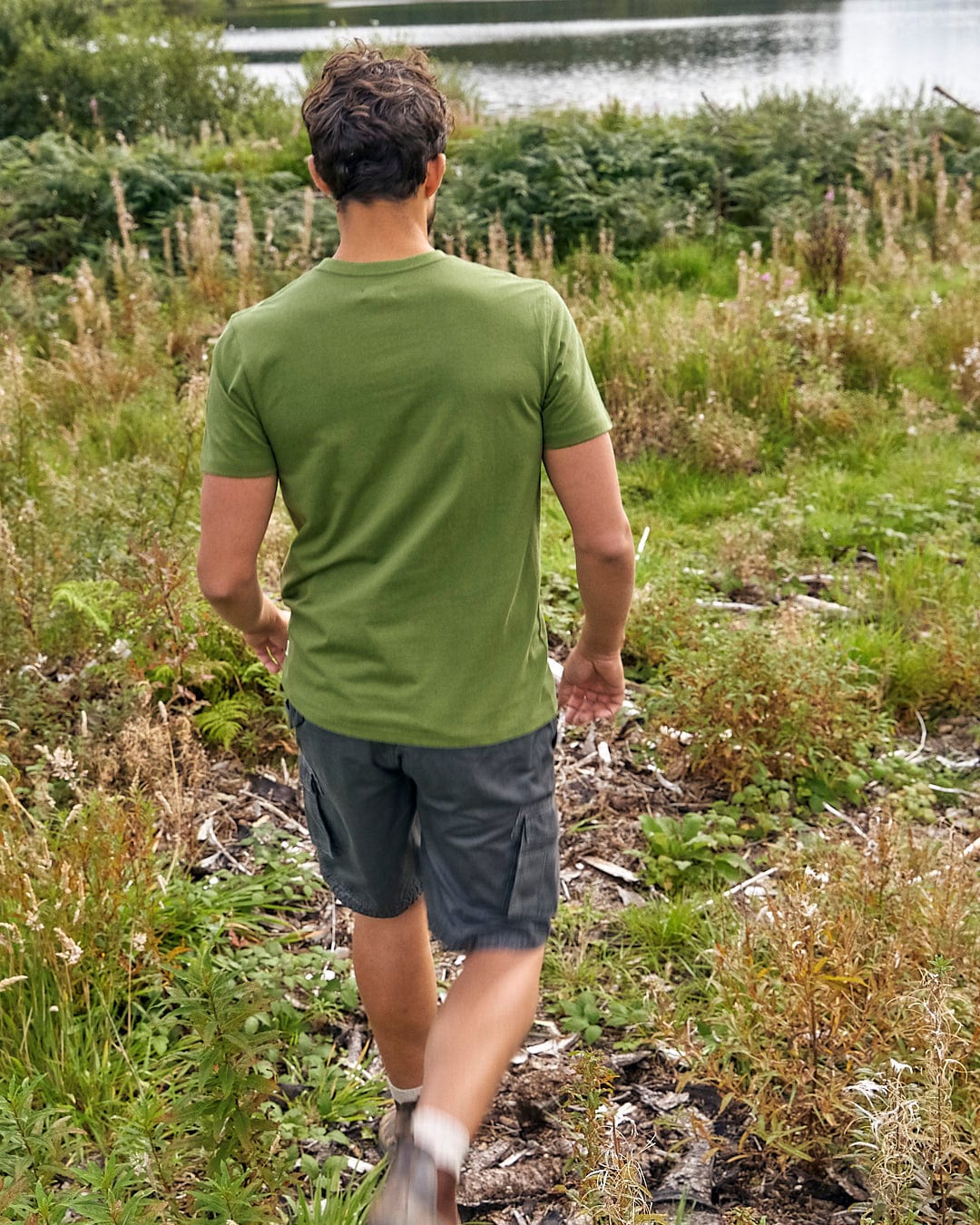 A man in a Trail Bike - Mens Short Sleeve T-Shirt - Green, sporting Saltrock branding, walking through a grassy area.