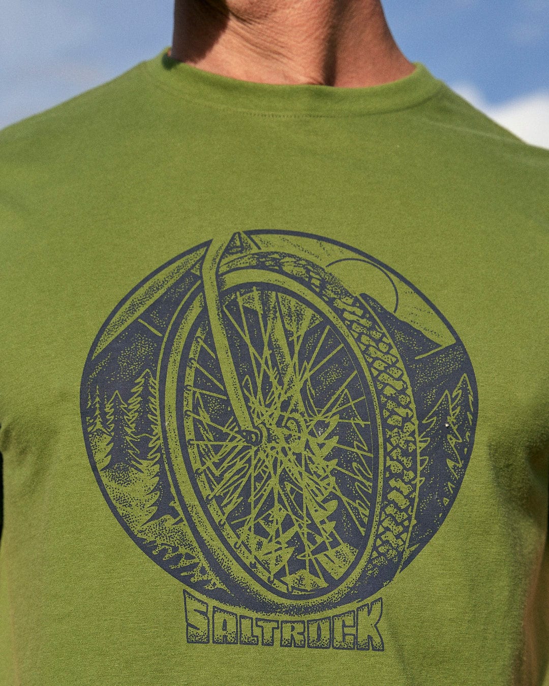 A man wearing a Saltrock Trail Bike - Mens Short Sleeve T-Shirt - Green with a bicycle wheel design.