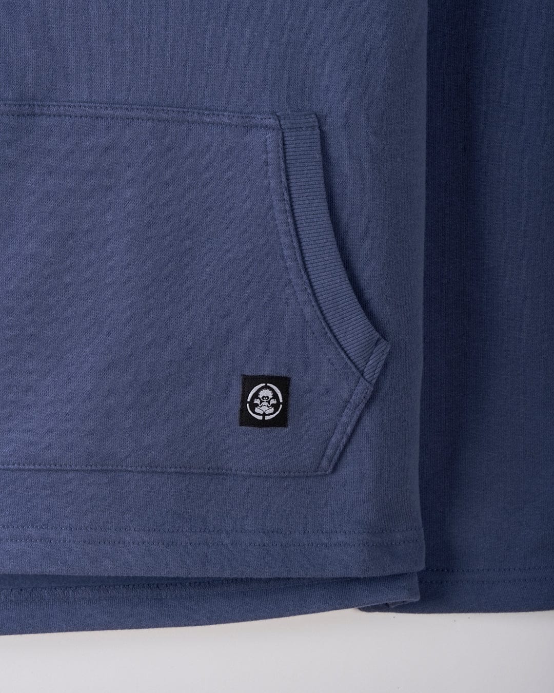A close-up of the Tribal SR Kids Recycled Pop Hoodie in blue, featuring a kangaroo pocket and a small black label with the white Saltrock logo.