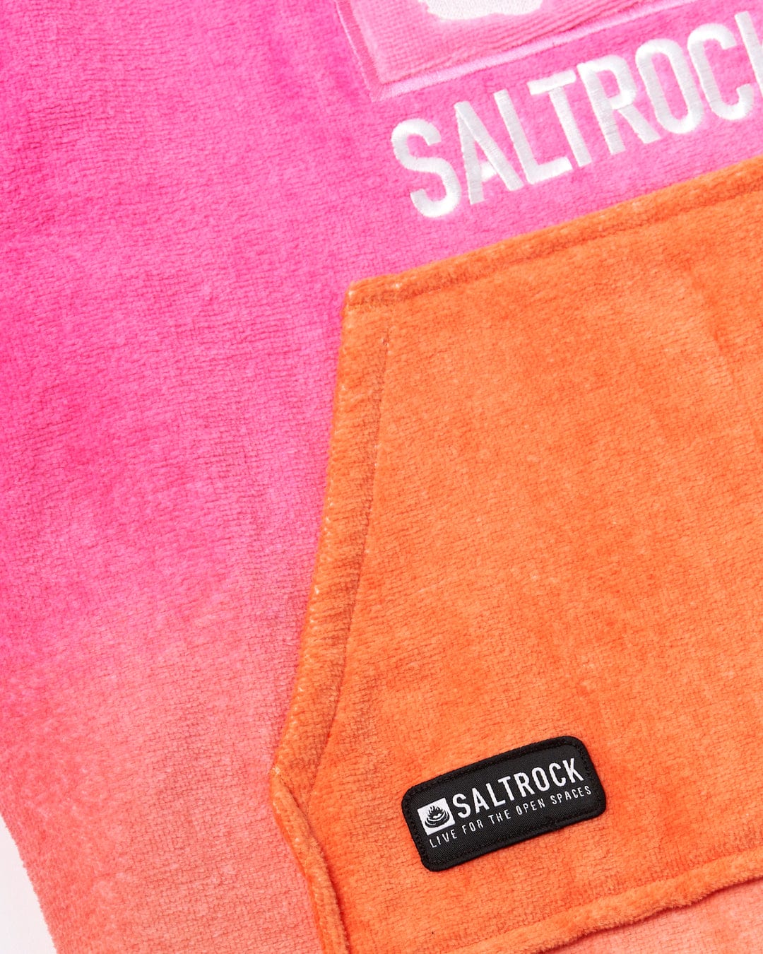 Close-up of a Tropic Dip - Kids Changing Towel - Pink/Orange partially overlaid with an orange pocket featuring a black Saltrock logo patch.